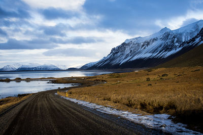 Road by snowcapped mountains against sky during winter