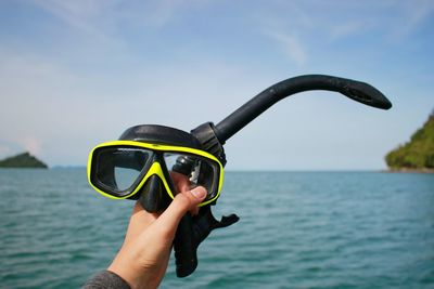 Cropped hand of person holding snorkel against sea and sky