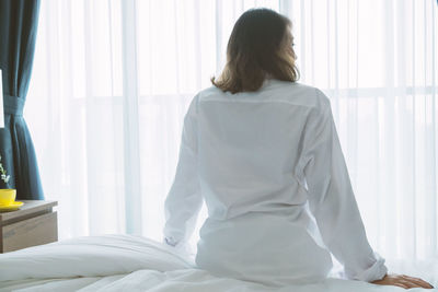 Rear view of woman sitting on bed at home