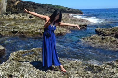 Woman with arms raised on rocks at beach