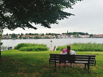 Rear view of woman sitting on riverbank against sky