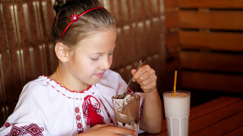 Happy smiling teen girl, child eats ice cream in a cafe. she is dressed in ukrainian national