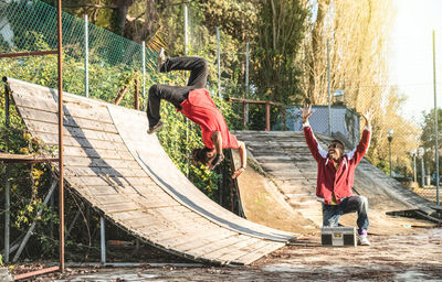 Man with male friend backflipping on ramp at public park