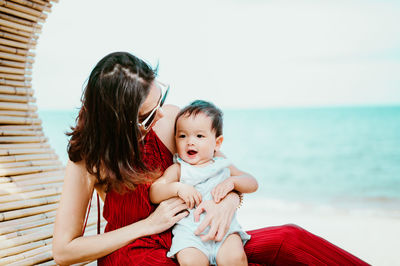 Mother and son relaxing at beach against sky