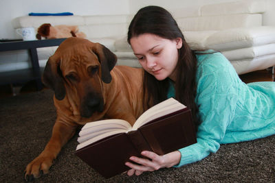 Young woman reading book with dog at home