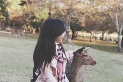 Side view of young woman with deer on field