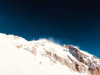 Low angle view of snowcapped mountain against clear blue sky