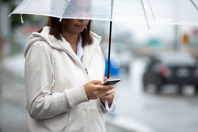 Woman holding mobile and umbrella on the street