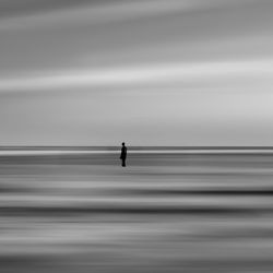 Silhouette person standing on sea against sky