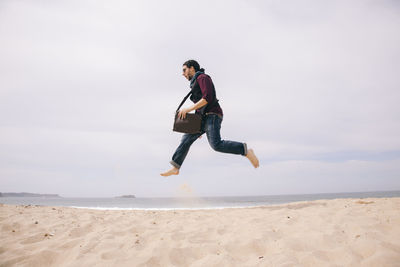 Full length of man jumping on beach against sky