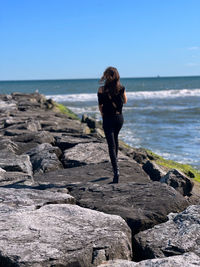 Rear view of woman standing at beach against clear sky