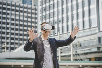 Businessman looking through virtual reality simulator while standing against building