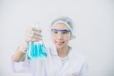 Scientist holding beaker with blue liquid standing against white background