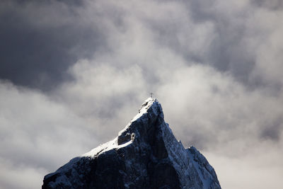 Dramatic view of mountain peak with summit cross against stormy clouds