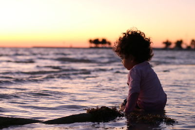 Boy looking at sea against sky during sunset