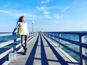 Woman sitting on railing by sea against sky