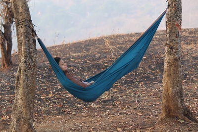 Young woman looking away while resting in hammock at forest