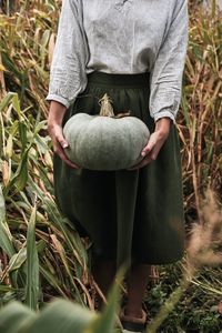 Midsection of woman holding pumpkin while standing in farm