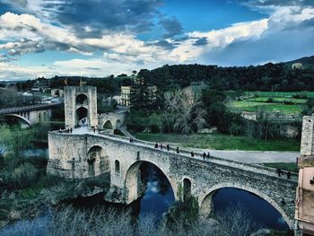 Arch bridge over river in city against sky