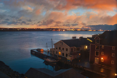 Buildings by sea against sky at sunset