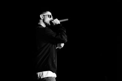 Side view of young man singing against black background