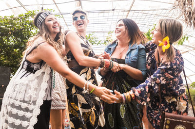 Low angle view of cheerful female friends standing in greenhouse