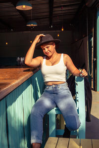 Midsection of young woman holding hat while standing against wall