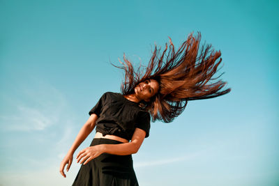 Low angle view of woman tossing hair against clear sky