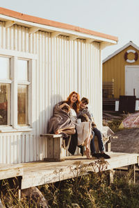 Portrait of smiling mother and son bonding while sitting against cabin during sunny day