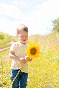 Little cute boy in a field of sunflowers in a yellow t-shirt stands and smiles.