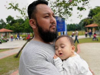Smiling father carrying baby while standing in park