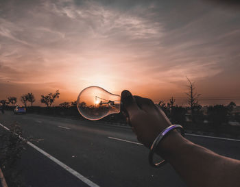 Close-up of hand on road against sky during sunset