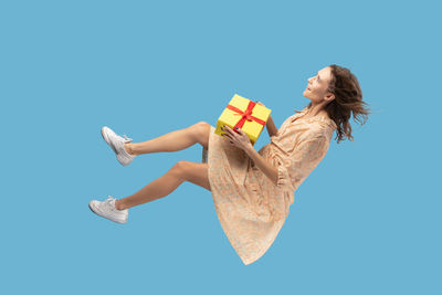 Full length of woman with gift box levitating against blue background