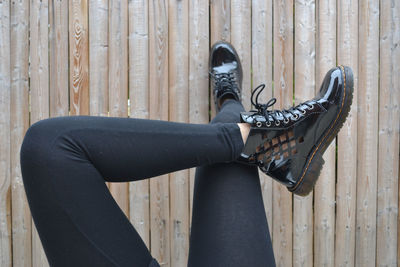 Low section of woman with legs crossed at knee against wooden fence