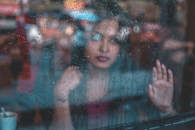Portrait of woman looking through wet window in rainy season