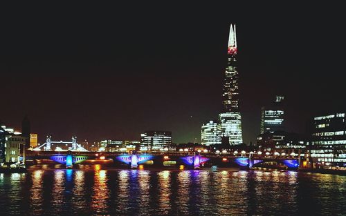 Illuminated city by river against sky at night