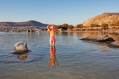 Rear view of woman standing in water against clear sky