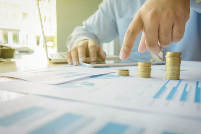 Midsection of businessman with coins on graph at desk in office