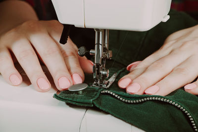 Woman designer or tailor working on sewing machine. hands hold and sew on details of clothing.