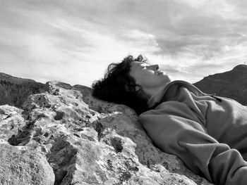 Woman lying down on rock against sky