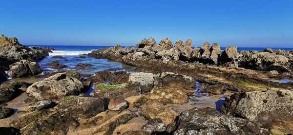 Scenic view of rocks in sea against clear blue sky