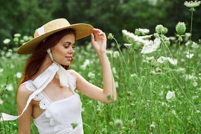 Side view of woman wearing hat standing against plants