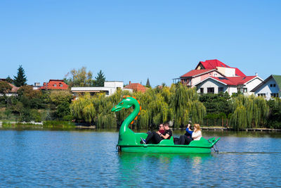 People on lake by houses against clear sky