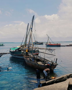 Men standing by boats moored on sea against sky