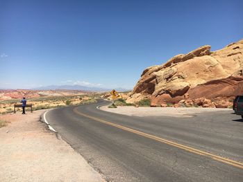 Road leading towards mountains against clear blue sky