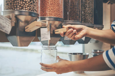 Hands of woman holding mason jar under food dispenser in store