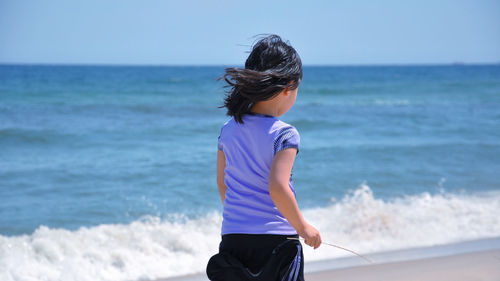 Rear view of girl on beach against sea