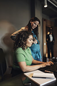 Businesswoman working on laptop by female pregnant colleague in office