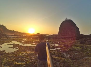 Rear view of man standing on land against sky during sunset