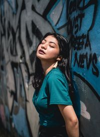 Beautiful young woman standing against graffiti wall